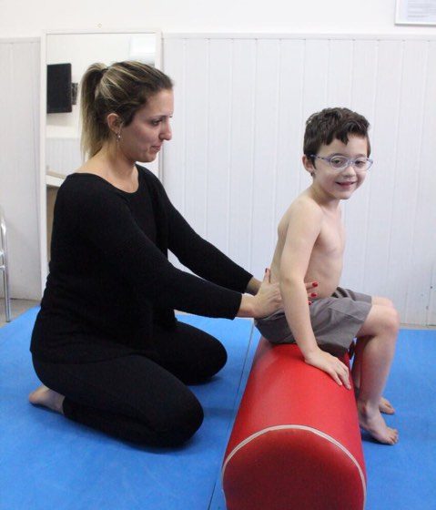 fisioterapeuta segurando o quadril de uma criança sentada no rolo de fisioterapia