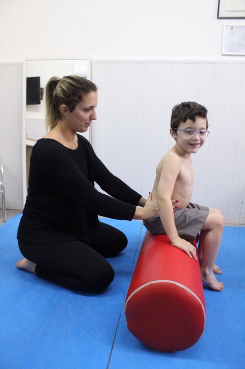 fisioterapeuta segurando o quadril de uma criança sentada no rolo de fisioterapia
